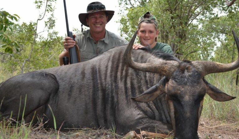 Man and boy posing with a blue wildebeest hunting trophy.