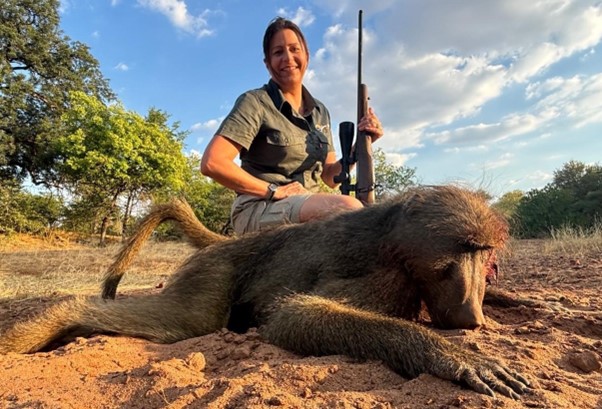Lady hunter posing with her gun and the baboon she shot.