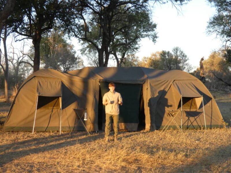 A boy standing in front of a canvas tent in the bush